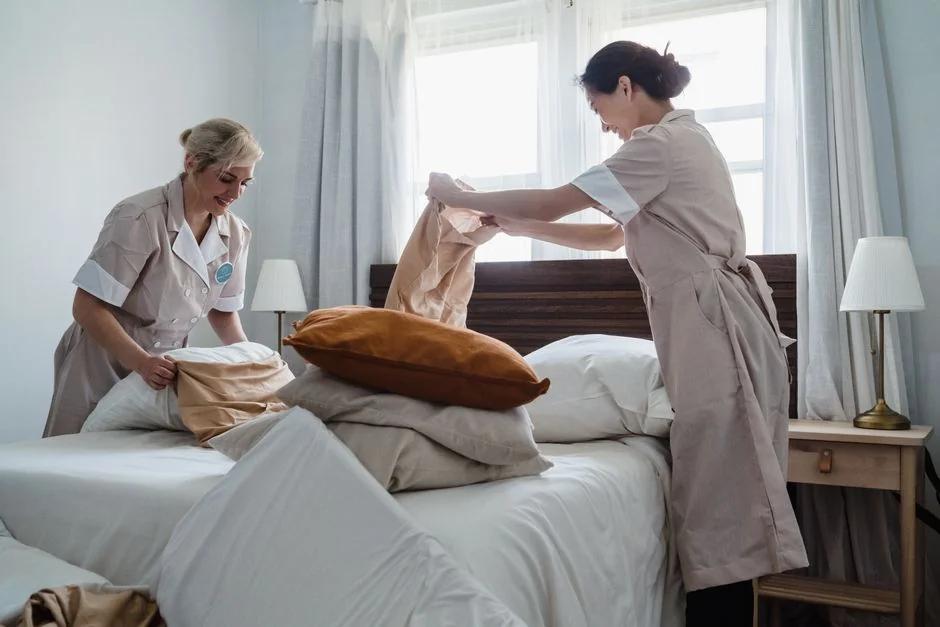 Crop anonymous female housewife in rubber gloves dusting modern lamp with soft brush against mirror while cleaning stylish bathroom